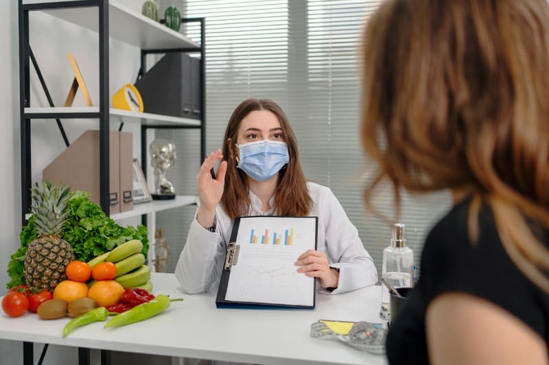 profissional-da-faculdade-de-nutricao-atendendo-moca-mostrando-indices-caloricos-em-uma-prancheta