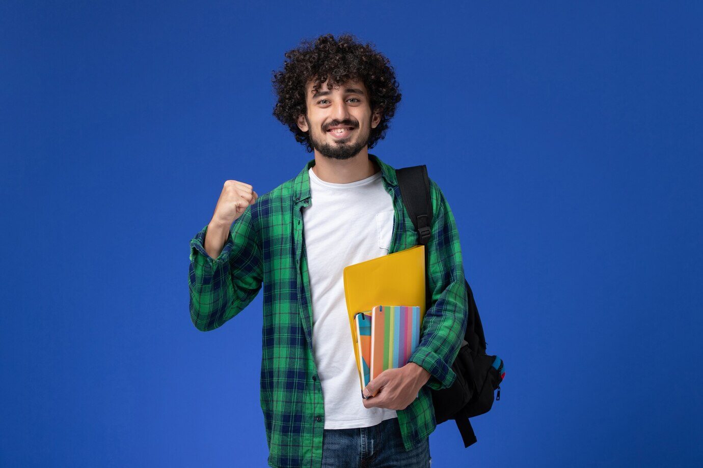 estudante-usando-uma-mochila-preta-segurando-cadernos-e-arquivos-na-parede-azul